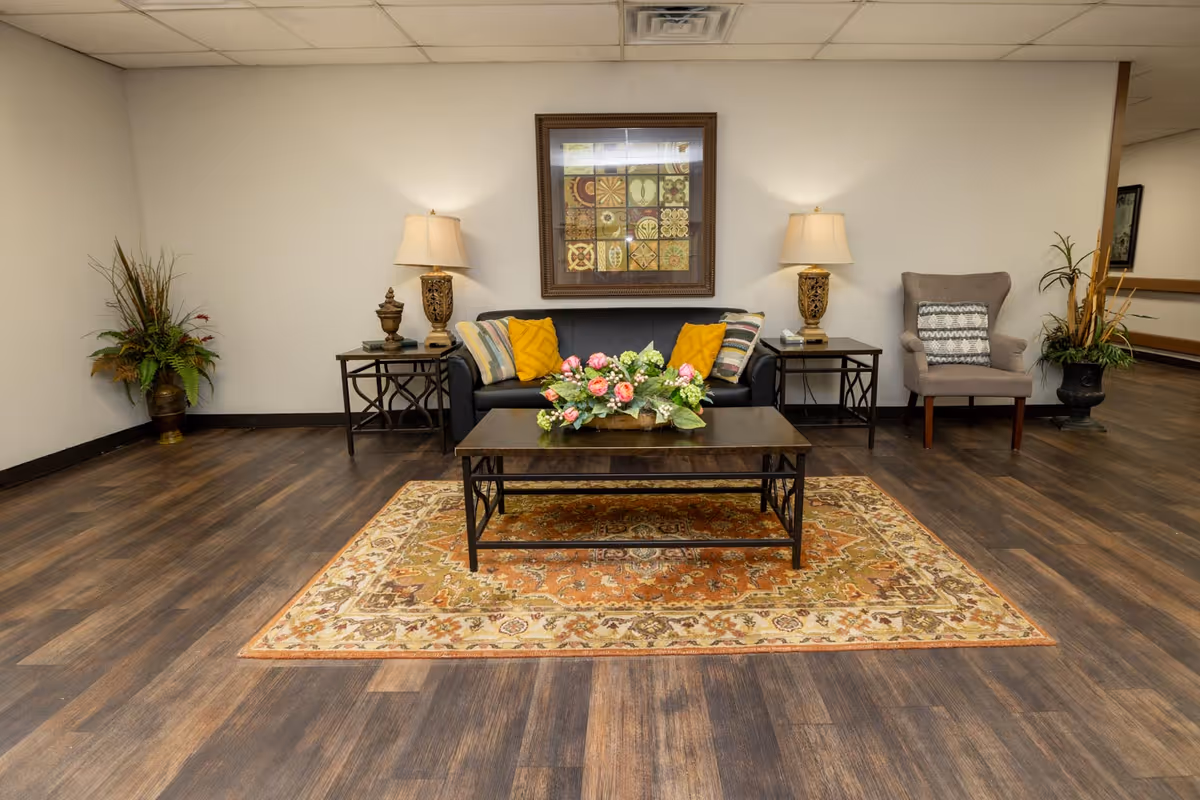 Lobby seating area with a sofa, armchair, coffee table topped by a floral arrangement, side tables with lamps, and framed wall art.