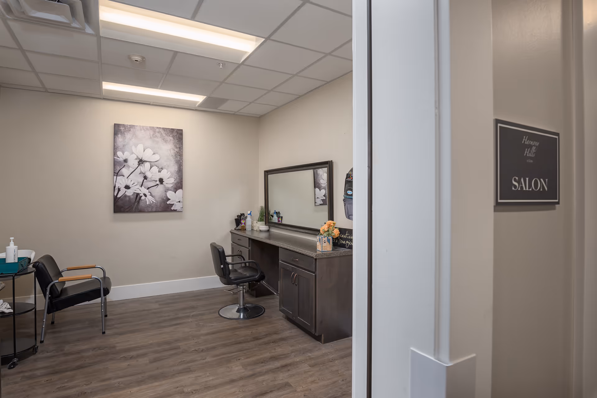 Interior view of a small salon with styling chairs, a mirror and floral wall art.
