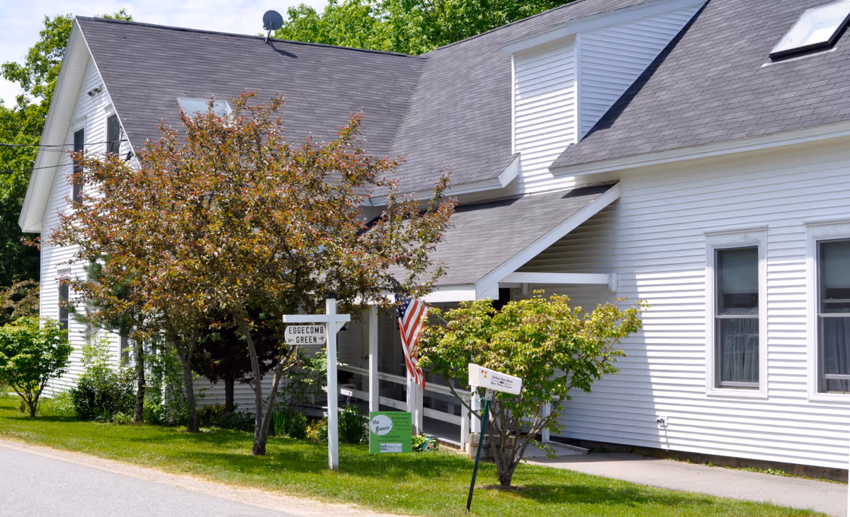 Front exterior of a white building with trees, an American flag, and a sign reading 'Edgecomb Green'.