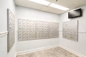 A small interior mailroom with rows of metal mailboxes mounted on light blue walls and a flat-screen TV in the corner.