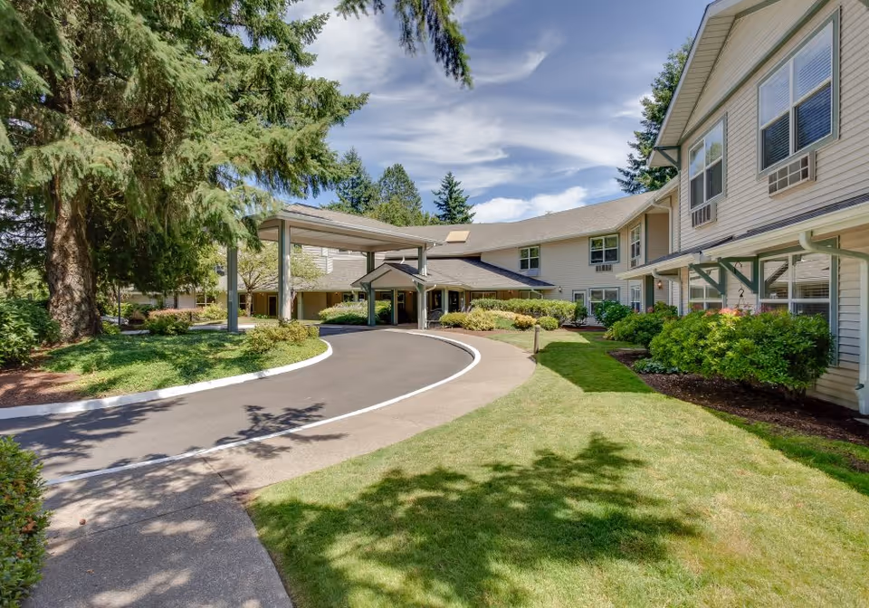 Front entrance of a senior living building with a covered porte-cochère, circular driveway and landscaped lawn.