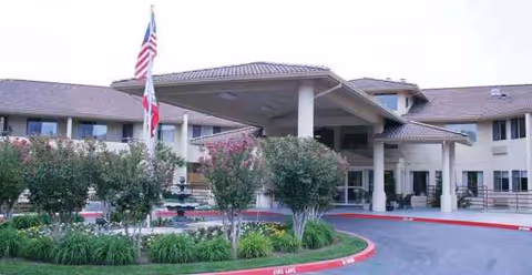 The front entrance of Truewood by Merrill, Fig Garden, with a porte-cochere, flags, and landscaping.