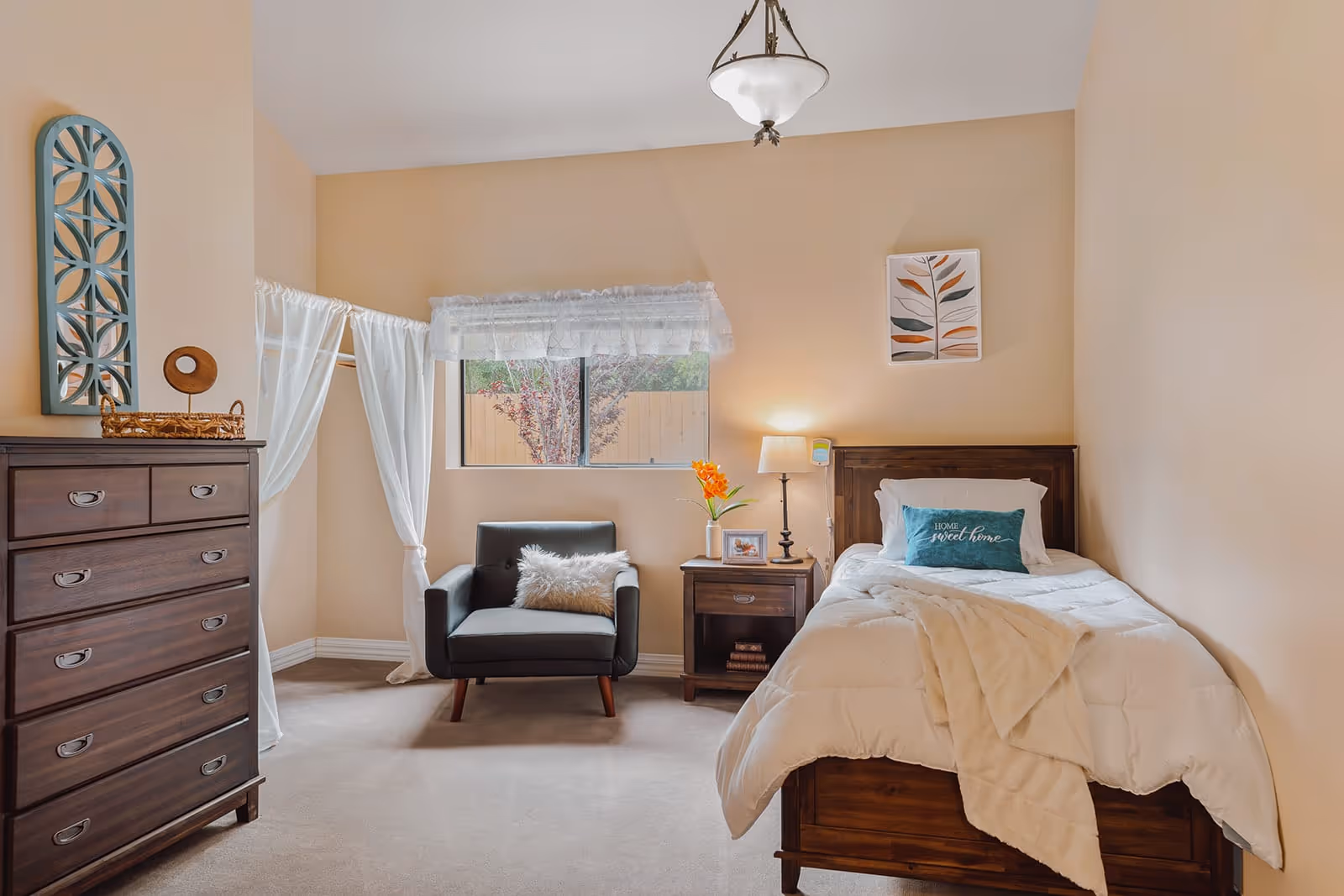 Well-lit bedroom with a single bed, nightstand, armchair and dresser under a window.