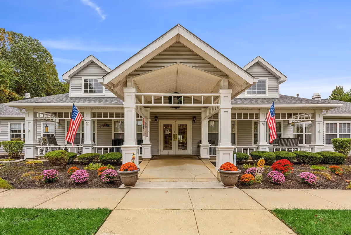Front entrance of Summit Place senior living building with a covered porte-cochere, American flags, and landscaped flowerbeds.