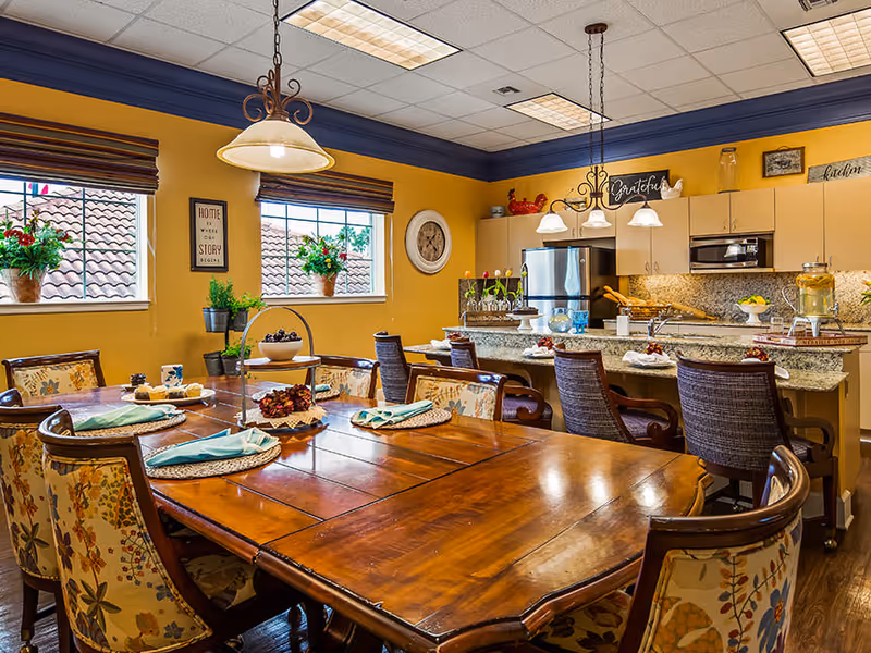 Warmly decorated communal dining area with a large wooden table set for a meal and an open kitchen in the background.