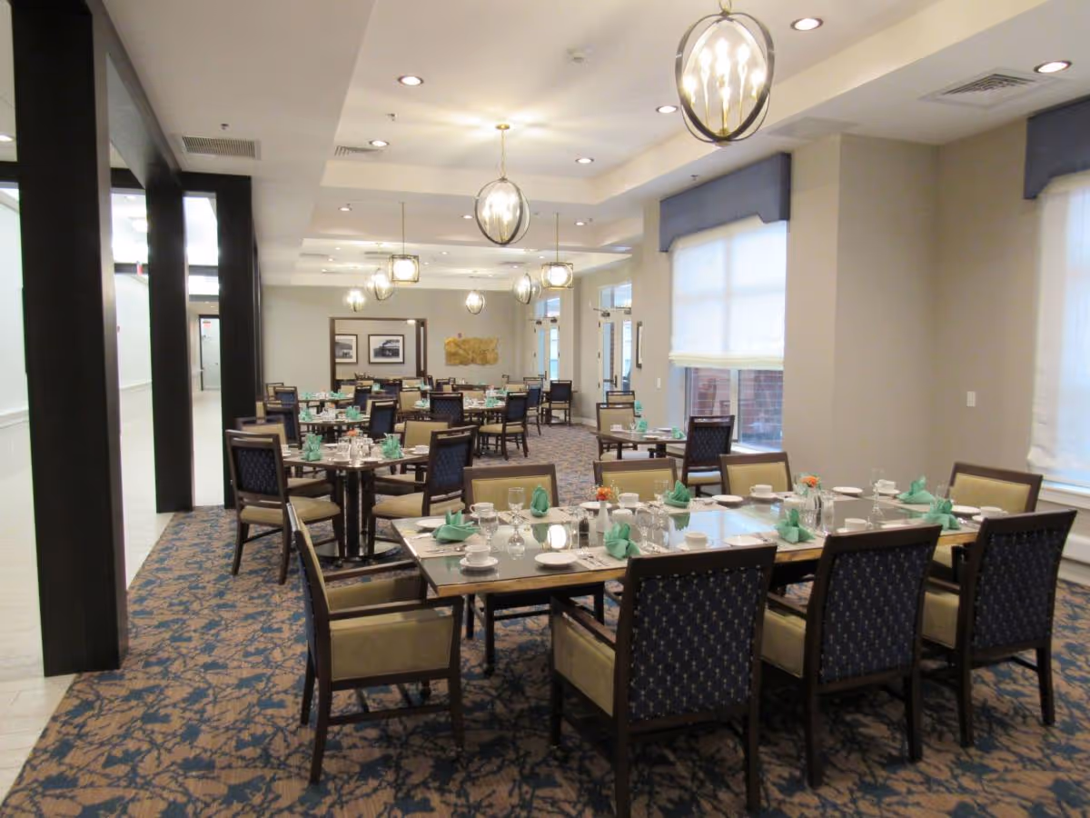 Spacious dining room with multiple set tables and chairs, pendant lights, and patterned carpet.
