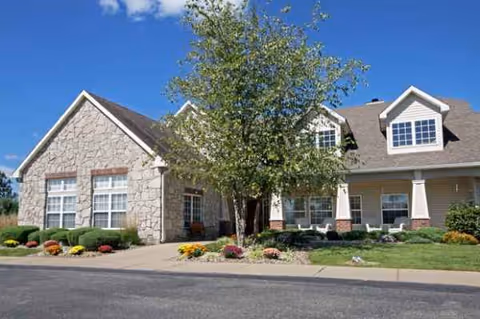 A senior living facility building with stone facade, a tree, and manicured landscaping in front.