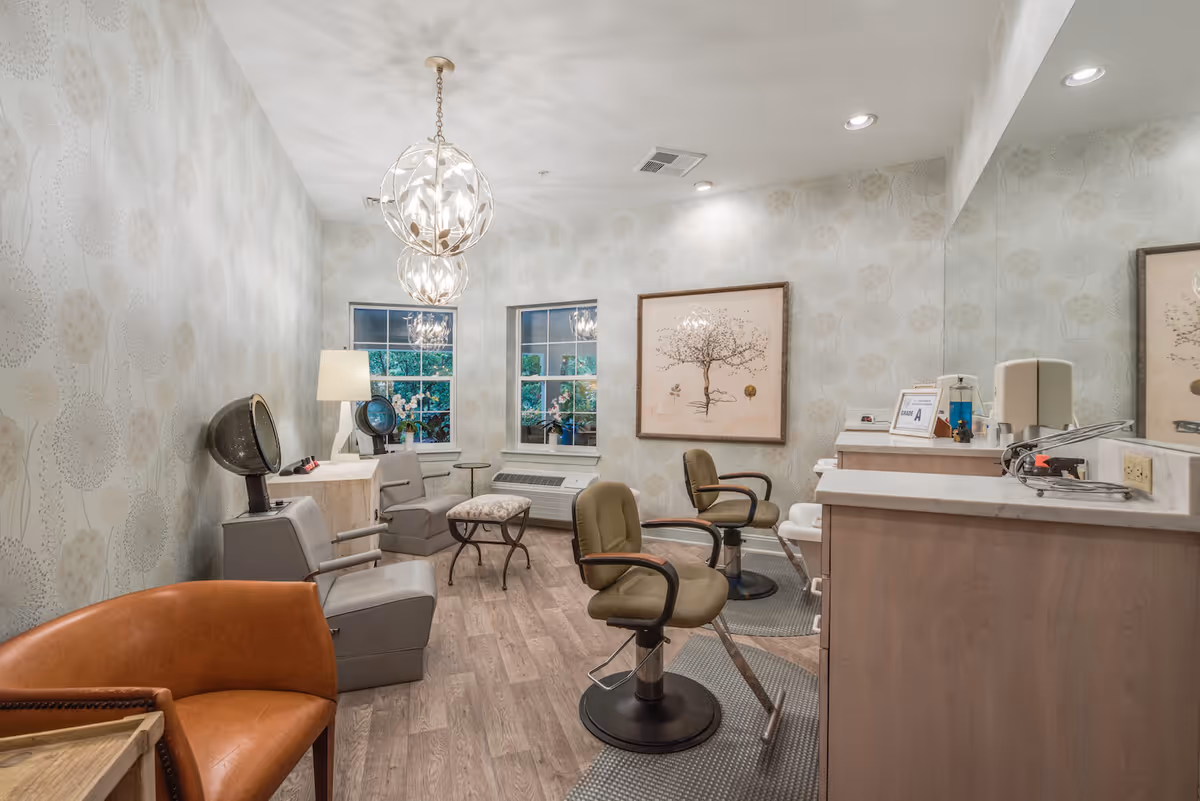 Well-lit interior salon room with styling chairs, hair dryers, wash sinks, decorative lighting, and framed artwork.