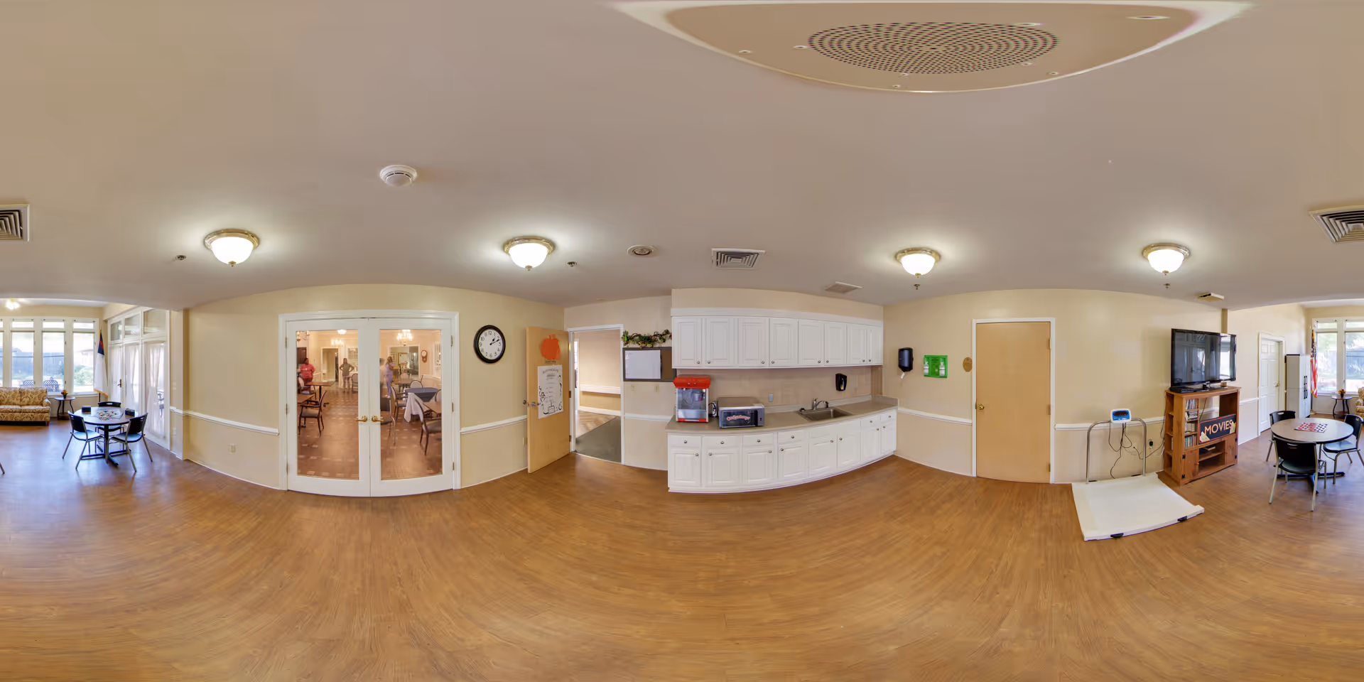 Community common area with a kitchenette, seating tables, TV, and double glass doors.