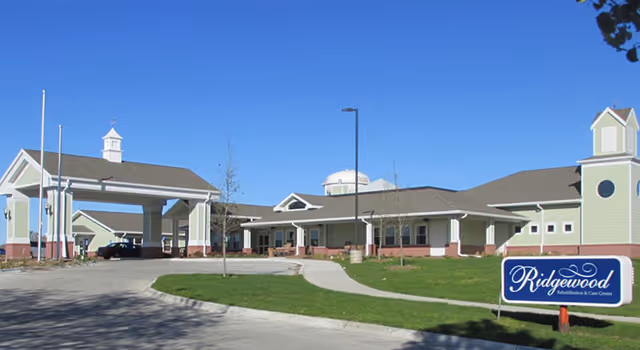 Front exterior of Ridgewood Rehab & Care Center showing a covered drop-off entrance, lawn, and a sign reading 'Ridgewood'.