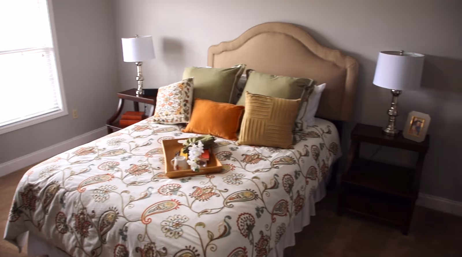 A neatly made bed with a patterned quilt, decorative pillows, bedside tables and lamps in a softly lit bedroom.
