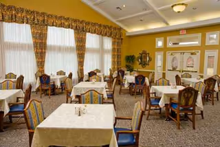 A well-lit dining hall with tables, chairs, and large curtained windows.