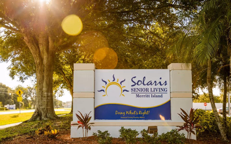 Outdoor entrance sign for Solaris Senior Living Merritt Island surrounded by landscaping and trees with sunlight lens flare.