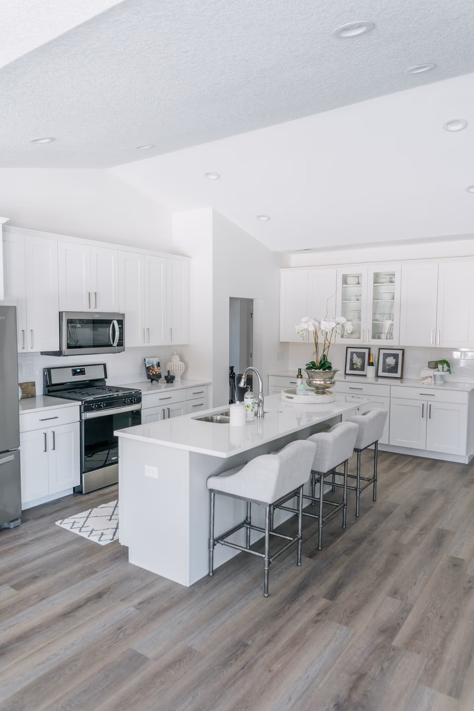 Bright modern kitchen with a large island, four upholstered bar stools, white cabinetry, and stainless steel appliances.