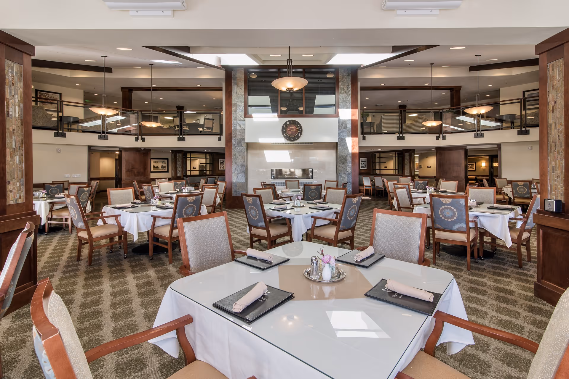 Spacious dining hall with round and square tables, white tablecloths, warm lighting.