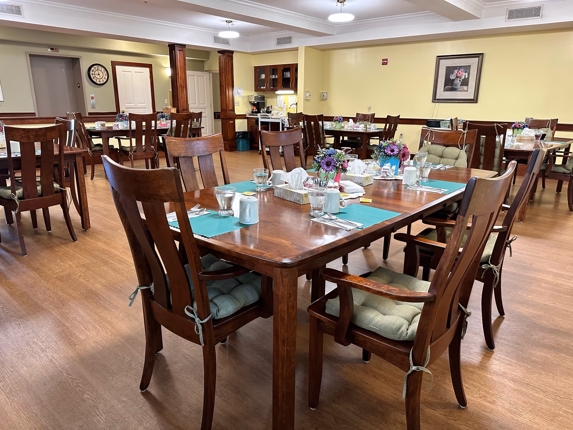 Dining room with wooden tables and chairs set with place settings and floral centerpieces.