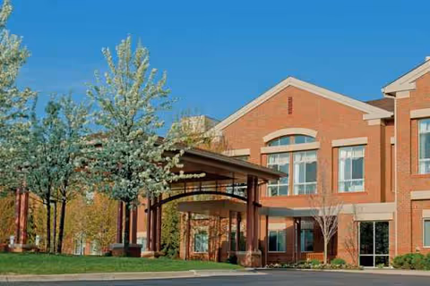 Fox Run Village brick senior living building with covered entrance and trees against blue sky.