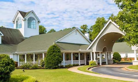 Exterior view of a senior living facility with curved porte-cochere and green landscaping.
