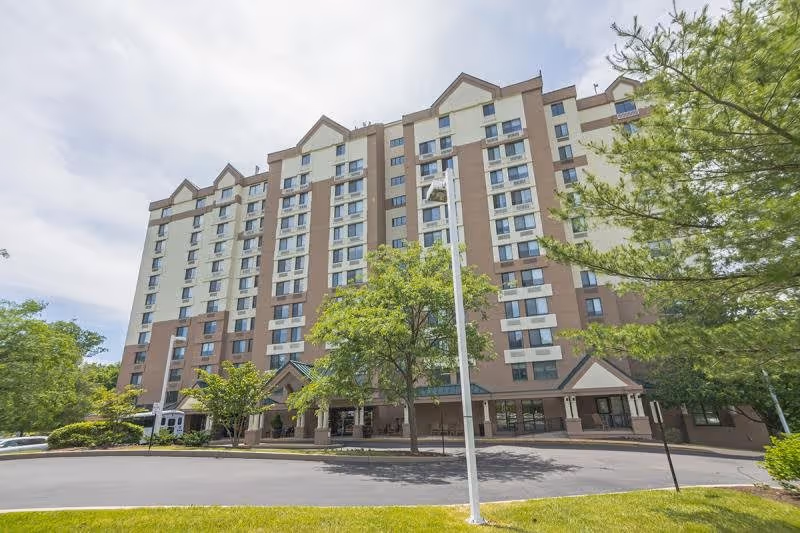 Exterior view of a multi-story senior living facility building named Chestnut Ridge Wallingford, surrounded by trees and greenery under a partly cloudy sky.