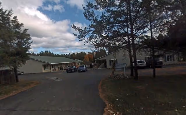 Exterior view of Cedar Creek Manor with driveway, trees, and parked cars.