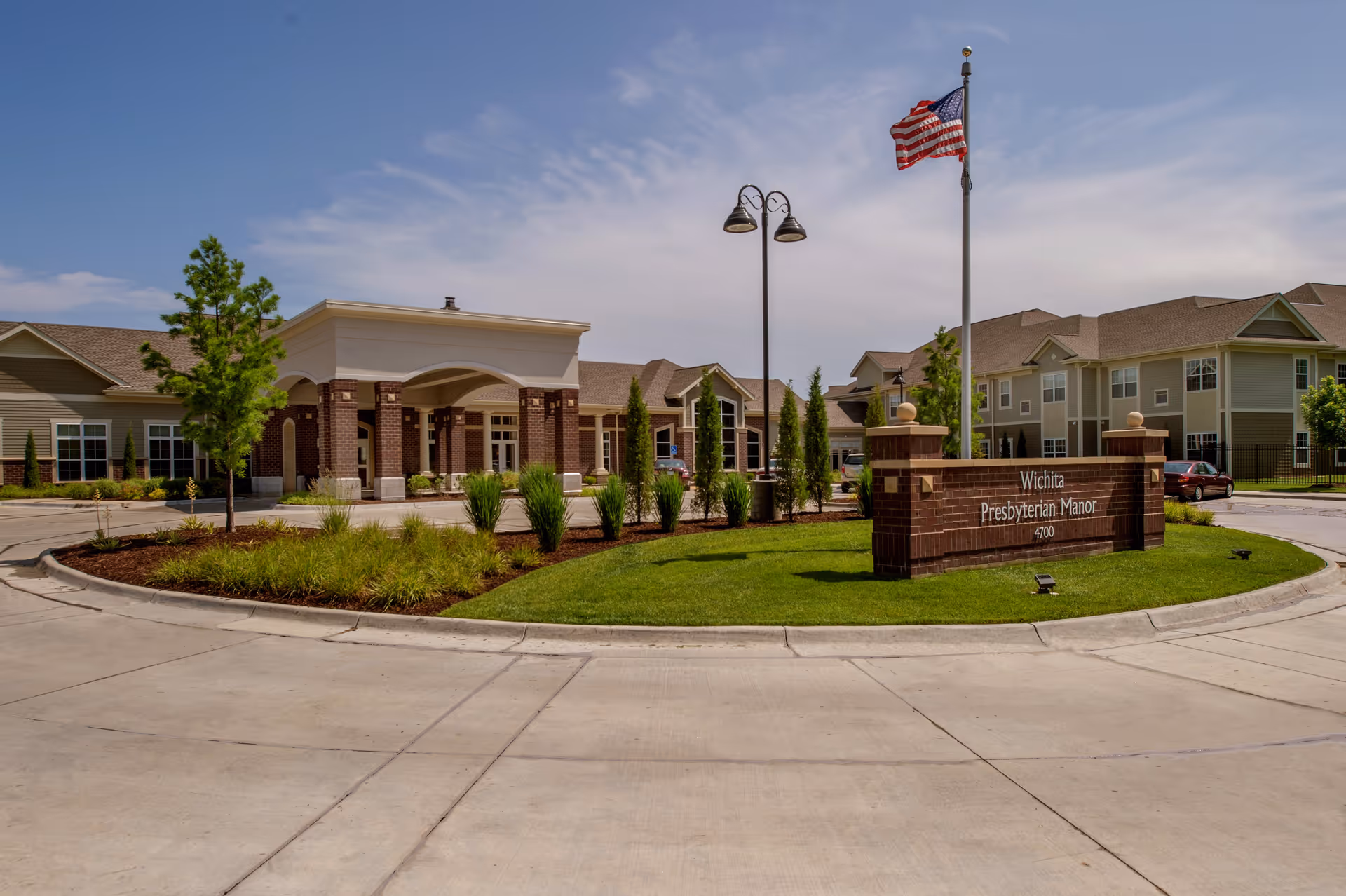 Front entrance of Wichita Presbyterian Manor with a circular driveway, landscaped island, American flag, and the building facade.