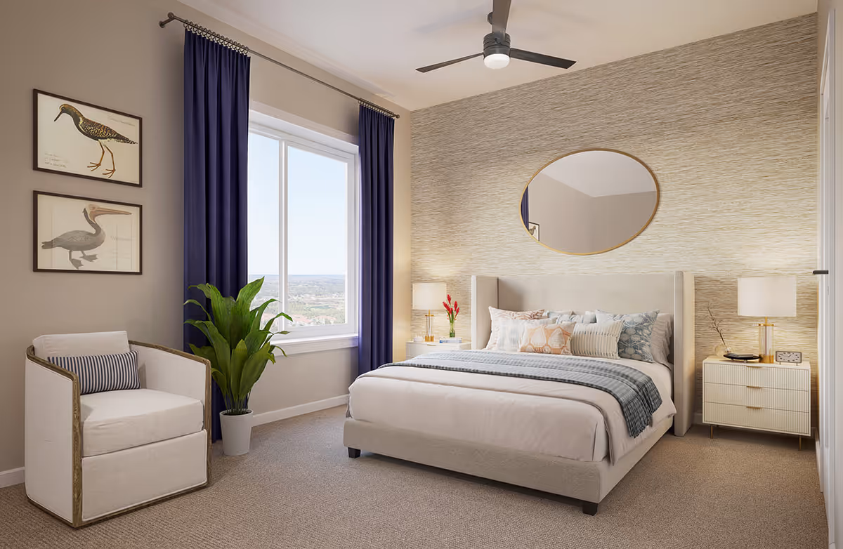 A bright and cozy bedroom featuring a large bed with multiple decorative pillows and a blue throw blanket. On either side of the bed are matching nightstands with lamps. A round mirror hangs above the bed on a textured accent wall. To the left, there is a comfortable armchair with a striped pillow, a potted plant, and two framed bird illustrations on the wall. A large window with dark blue curtains lets in natural light and offers a view of the outdoors. A ceiling fan with a light fixture is mounted on the ceiling.