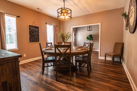 Round wooden dining table with chairs in a warmly lit, cozy dining room.