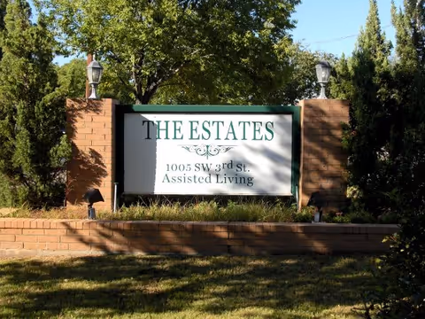 Brick entrance sign reading "THE ESTATES" with the address and "Assisted Living" surrounded by landscaping.