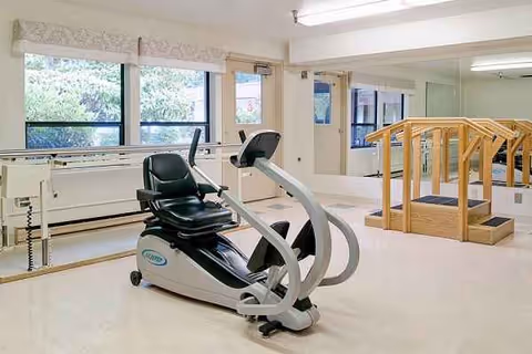 A compact rehabilitation gym with an elliptical trainer beside a wooden staircase.