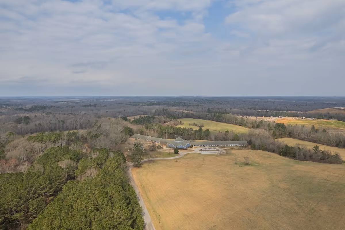 Aerial view of The Overlook Senior Living facility surrounded by expansive fields and wooded areas under a partly cloudy sky.