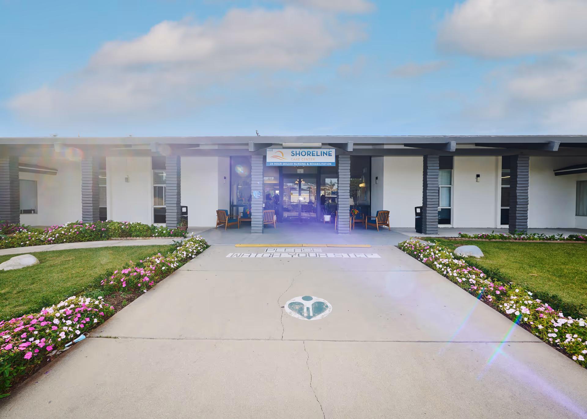 Front entrance of Shoreline Care Center showing a low building facade, walkway flanked by flower beds, and a sign reading "SHORELINE".