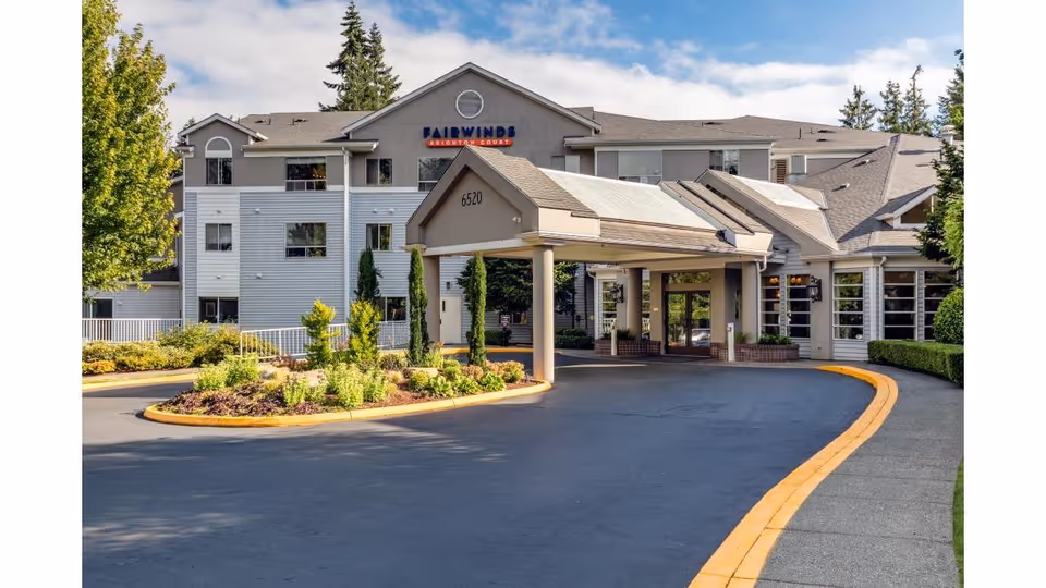 Front entrance and porte-cochère of the Fairwinds Brighton Court building with a circular driveway and landscaped island.
