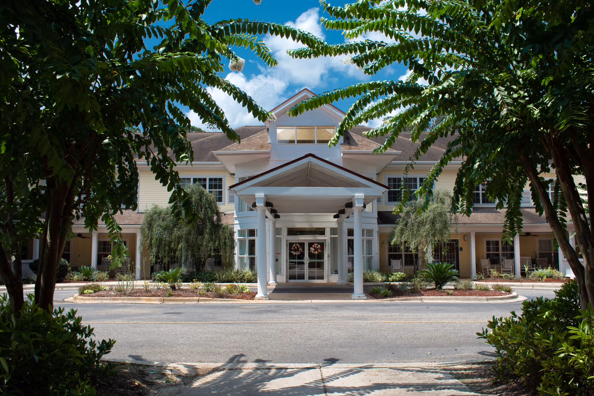 Front entrance of a two-story residential building with a covered porte-cochère framed by trees.