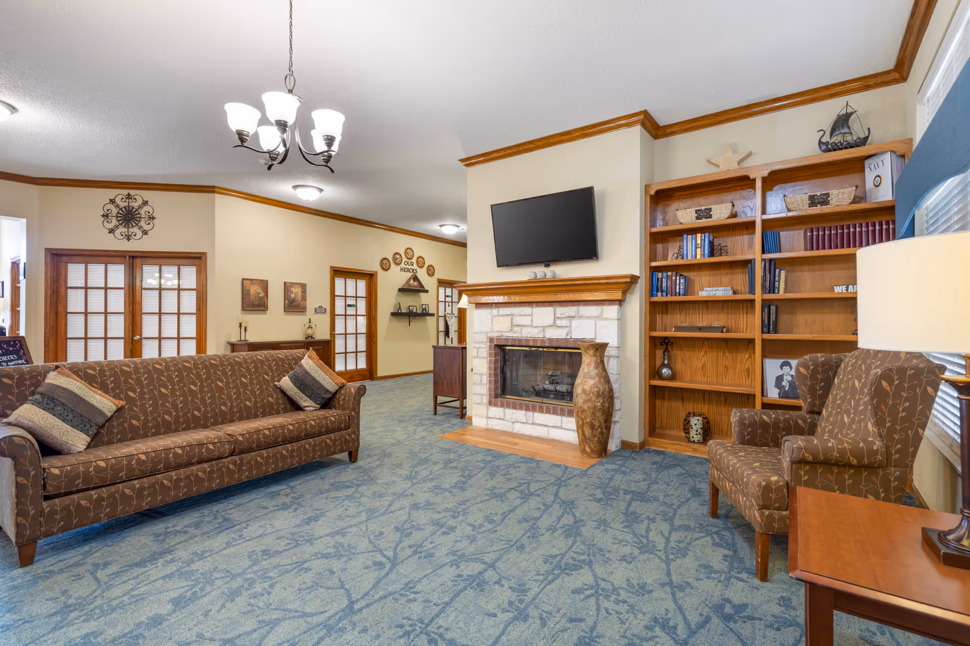 A cozy lounge with patterned sofas and an armchair facing a stone fireplace with a wall-mounted TV and built-in bookshelves.
