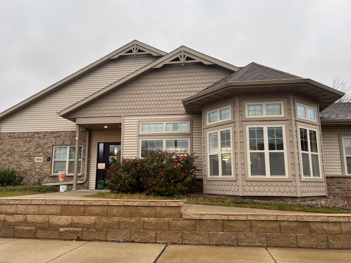 Front exterior of a single-story senior living building showing an entrance, bay windows, and landscaping.