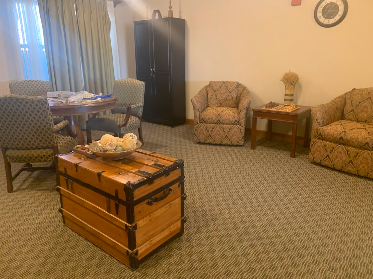 Communal sitting area with patterned armchairs, a round table, a wooden trunk used as a coffee table, and an armoire.