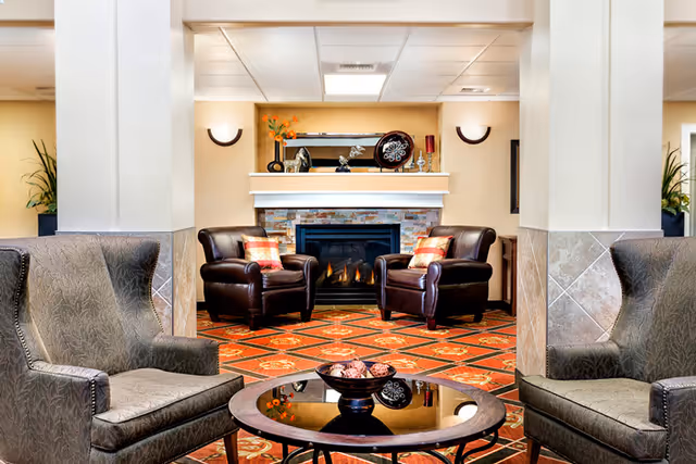 Comfortable lounge with armchairs and a coffee table facing a fireplace and mantel decorations.