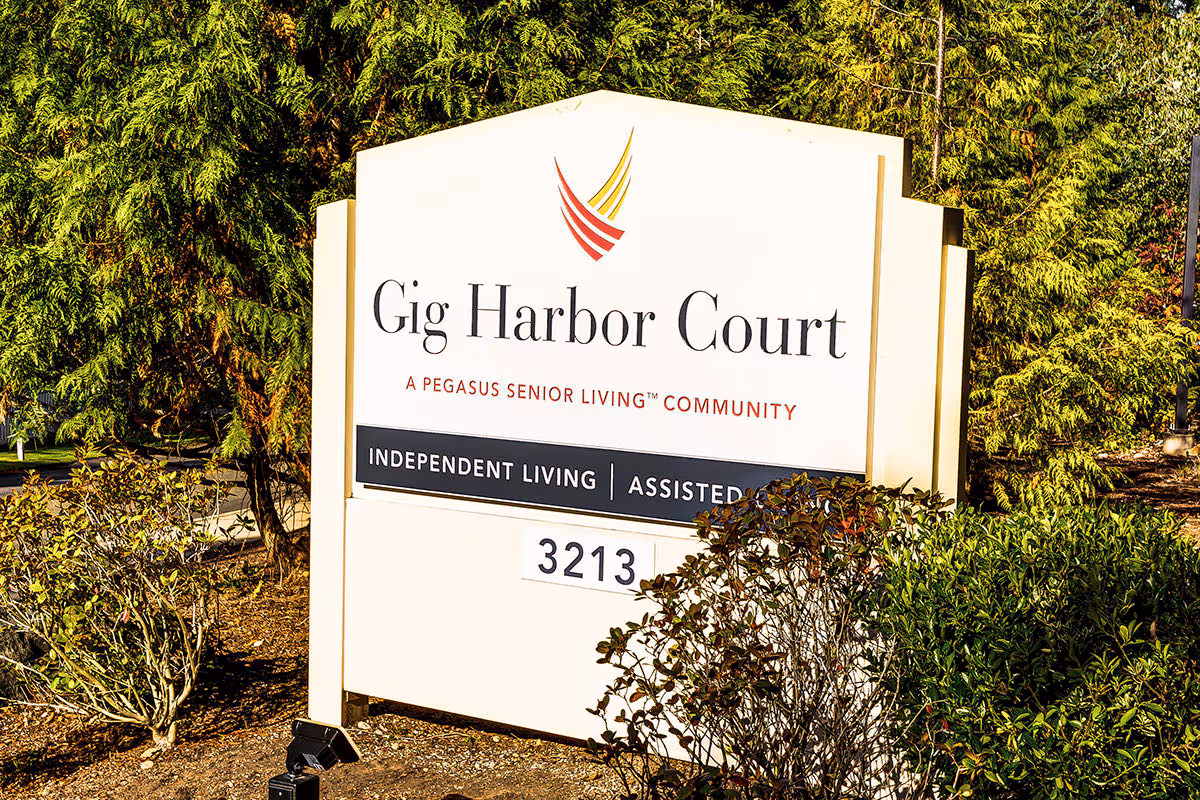 Outdoor sign for Gig Harbor Court, a Pegasus Senior Living community offering independent living and assisted living, surrounded by greenery and bushes.