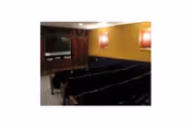 Small movie-theater style room with rows of upholstered seats facing a screen, yellow walls, and framed posters.