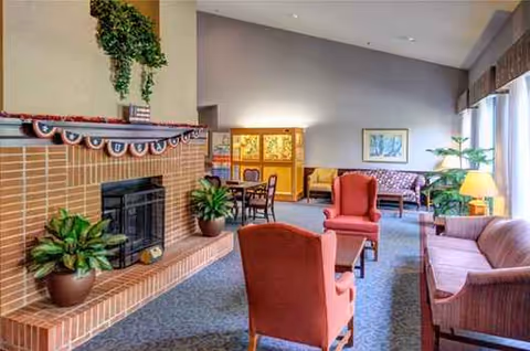 A cozy senior living lounge with a brick fireplace, plants, and comfortable seating.