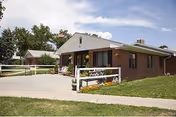 Single-story brick building with a small front porch, white railing, and green lawn.