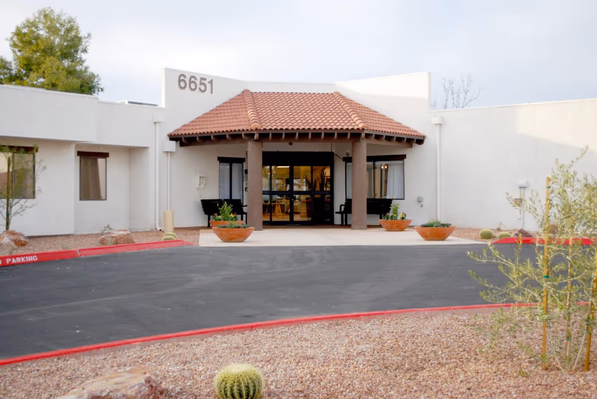 Front entrance of a single-story stucco building with a tile-roofed portico marked "6651", planters, and a driveway amid desert landscaping.