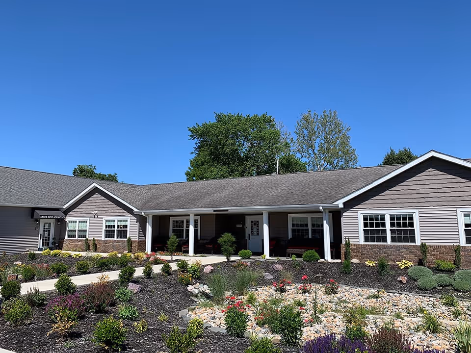 Exterior view of a single-story building with a gray roof and beige siding, surrounded by landscaped garden beds with various plants and flowers under a clear blue sky.