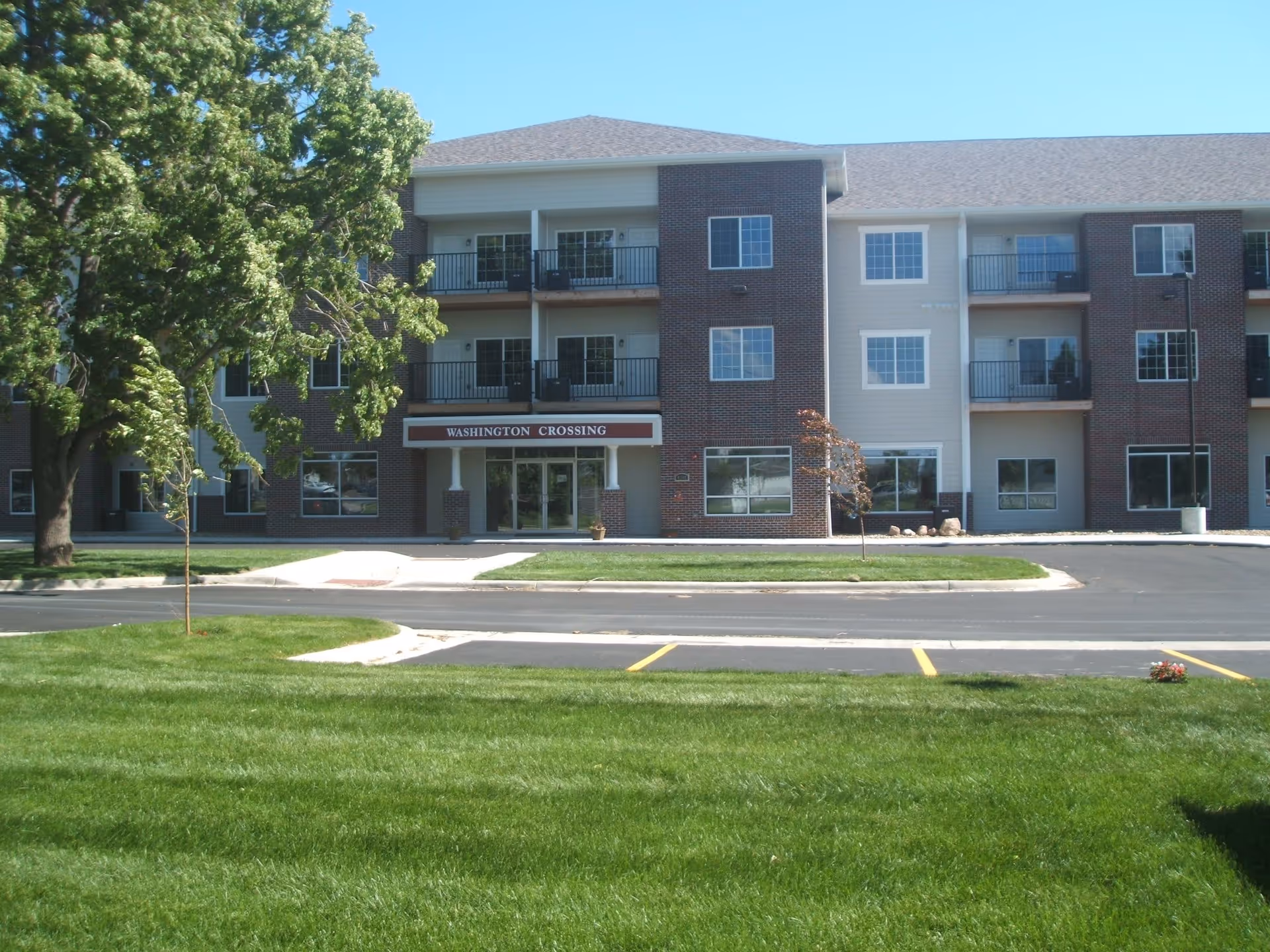 Exterior view of a three-story senior living facility named Washington Crossing with a well-maintained lawn, trees, and a parking area in front.