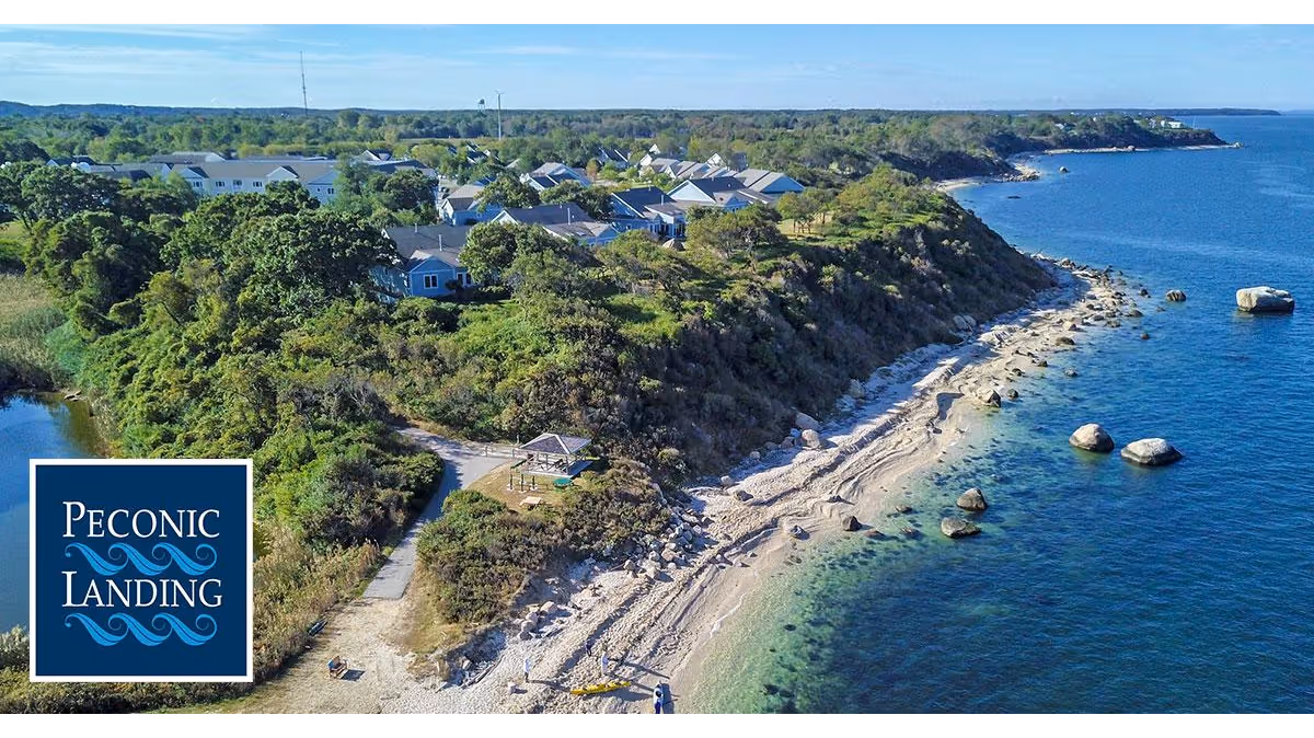Aerial view of Peconic Landing on a coastal bluff with homes, a small beach, and blue ocean.