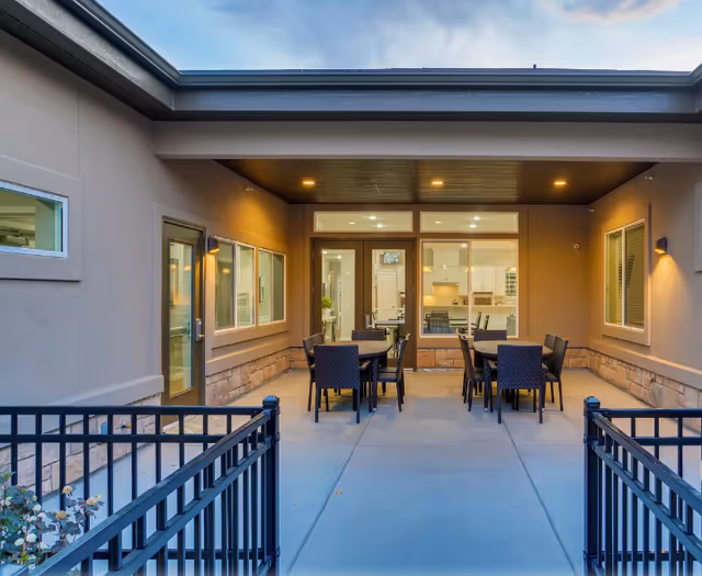 Covered outdoor patio with multiple dining tables and chairs leading to glass doors into the facility.