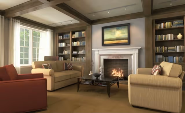 A cozy living room with a lit fireplace, two beige sofas with patterned pillows, a red armchair, a dark wooden coffee table, built-in bookshelves filled with books, and a large window with white curtains letting in natural light.