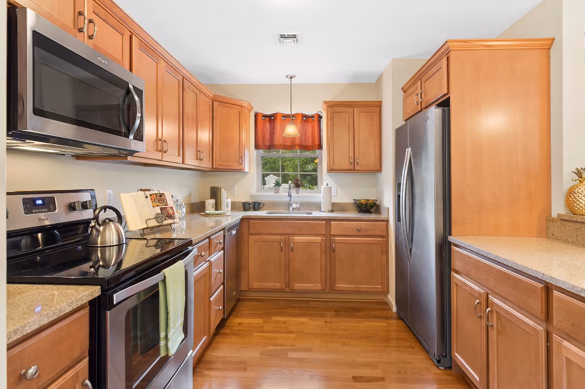 Bright kitchen with wooden cabinets, stainless steel appliances, and a window above the sink.
