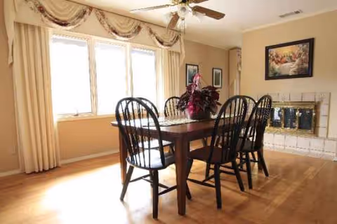 Sunlit dining room with a wooden table, six chairs, and a fireplace.