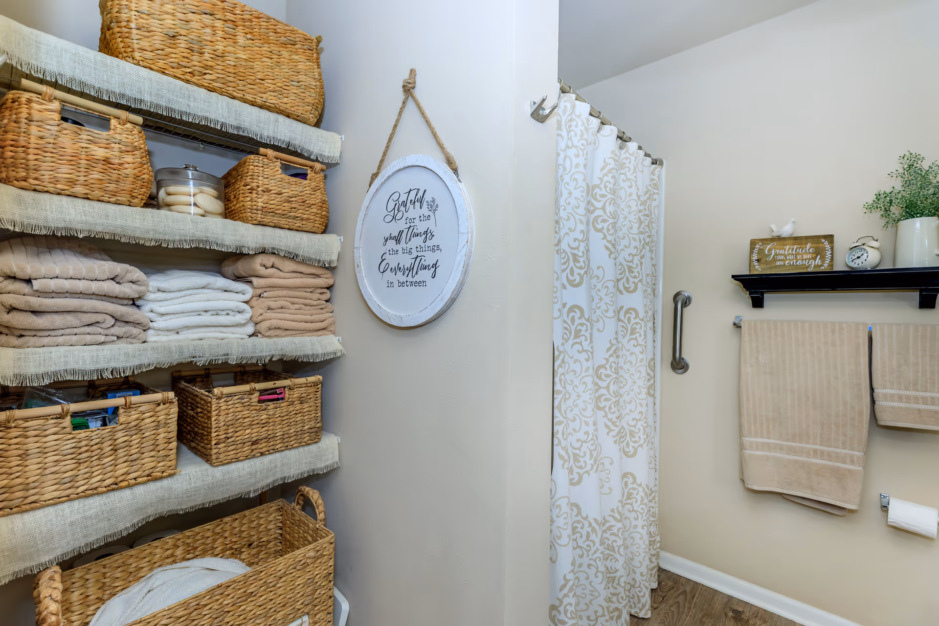 Neatly organized bathroom with woven baskets and folded towels on shelving, a patterned shower curtain, and a wall-mounted towel rack and grab bar.